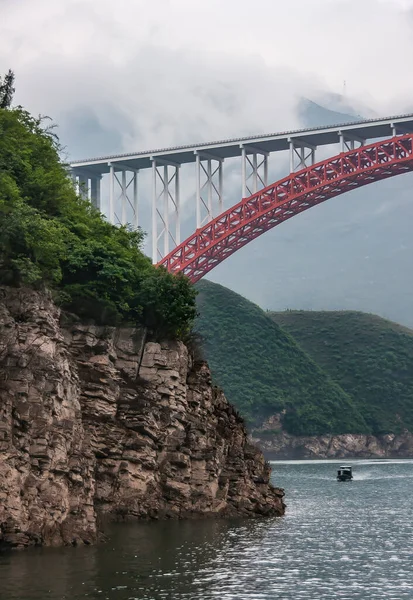 中国武昌 2010年5月7日 丹宁河龙门峡谷 红色的弓与平坦的白色混凝土路面桥之上的深绿色的水在雾蒙蒙的天空 山区海岸线和船只 — 图库照片