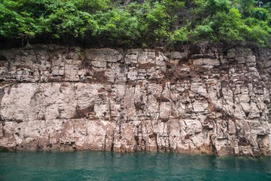 Wuchan, Çin - 7 Mayıs 2010: Daning Nehri 'ndeki Ejderha Kapısı Boğazı. Üzerinde kahverengi toprak ve yeşil yapraklar bulunan bej-kahverengi kayalık kıyı şeridi, zümrüt yeşili suyla iniyor..