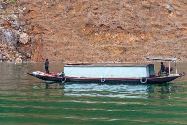 Wuchan, Çin - 7 Mayıs 2010: Daning Nehri 'ndeki Ejderha Kapısı Boğazı. Zümrüt yeşili sularda zümrüt yeşili iki kişilik açık mavi kulübe teknesi ve zemin olarak kayalık kahverengi kıyı şeridi..