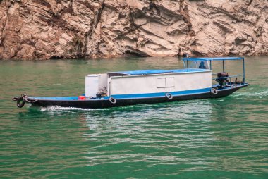 Wuchan, Çin - 7 Mayıs 2010: Daning Nehri üzerindeki Dawu veya Misty Gorge. Zümrüt yeşili su üzerinde seyahat eden küçük beyaz-mavi kulübe teknesinin yakınındaki zemin olarak kahverengi kayalık uçurum var..