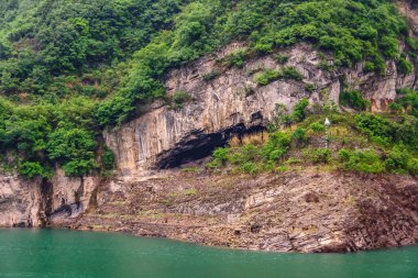 Zigui, Çin - 6 Mayıs 2010: Xiling vadisi Yangtze Nehri üzerinde. Yeşil suların üzerinde yeşil yapraklar olan kahverengi kaya kayalıklarında büyük bir mağara..