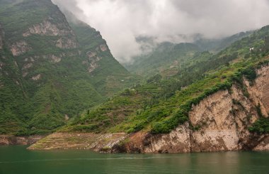 Xiangxicun, Çin - 6 Mayıs 2010: Xiling Vadisi Yangtze Nehri üzerinde. Teraslarda sıralanmış tarım arazileri yeşil sularda inen dağların yeşil yamaçlarını kapsıyor. Yoğun gri bulutlar iniyor.