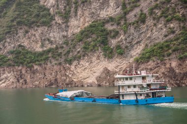 Xiangxicun, Çin - 6 Mayıs 2010: Xiling Vadisi Yangtze Nehri üzerinde. Mavi ve beyaz mavnada yüzen yeşil suyun derinliklerinde yükünü muşambalarla örtüyor. Kahverengi kaya kayalığı fon olarak.