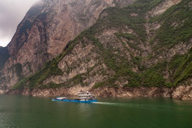 Xiangxicun, Çin - 6 Mayıs 2010: Xiling Vadisi Yangtze Nehri üzerinde. Mavi ve beyaz mavnada yüzen yeşil suyun derinliklerinde yükünü muşambalarla örtüyor. Kahverengi kaya kayalığı arka plan olarak. Bulutlar azalıyor.