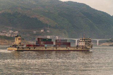 Xinling, Çin - 6 Mayıs 2010: Xiling vadisi Yangtze Nehri üzerinde. Bej rengi paslı konteynır teknesi, arkasında uzun yeşil dağlar ve yol köprüsü var..