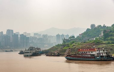 Fengdu, Chongqing, Çin - 8 Mayıs 2010: Yangtze Nehri. Bir grup eski, paslı tekne ve yeşil kıyı şeridi yakınlarındaki yüzen benzin istasyonunda yakıt ikmali. Şehir manzarası ve sisli gökyüzü diğer kıyıda.