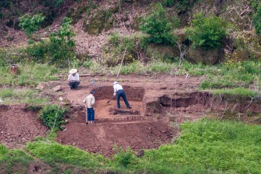 Fengdu, Chongqing, Çin - 8 Mayıs 2010: Yangtze Nehri. Kıyı şeridindeki yeşil bitki örtüsü arasında kahverengi toprak üzerinde çalışan çiftçilere yakın çekim.