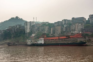 Myaoyinan, Chongqing, Çin - 8 Mayıs 2010: Yangtze Nehri. Kıyıda inşaat halindeki büyük nehir teknesinin kırmızı leşi var. Kahverengi suda 1 tamamlanmış. Tepedeki konut arkada..