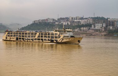 Myaoyinan, Chongqing, Çin - 8 Mayıs 2010: Yangtze Nehri. Koyu gri gökyüzünün altında şehir manzarası olan kahverengi sularda sarı yeni bir araba nakliye gemisi..