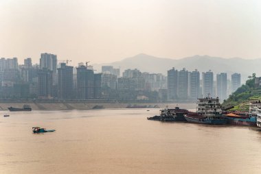 Fengdu, Chongqing, Çin - 8 Mayıs 2010: Yangtze Nehri. Kıyı şeridindeki yüksek binalar geniş kahverengi suların arkasında bazı gemiler yelken açıp demirlemiş. Sisli gökyüzü.