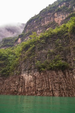 Wushan, Chongqing, Çin - 7 Mayıs 2010: Daning Nehri üzerindeki Mini Üç Boğaz. Beyaz bulutlar, zümrüt yeşili suyla dolu kanyondaki yeşil yapraklarla kahverengi kaya kayalıklarının üzerine iniyor..