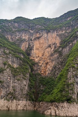 Guandukou, Hubei, Çin - 7 Mayıs 2010: Wu Gorge, Yangtze Nehri 'nde: Bulutların altında yeşil suyun üzerinde yeşil yapraklarla kaplı dağ yamaçlarında büyük bej rengi kahverengi kayalık kayalık kayalık kayalık kayalık.