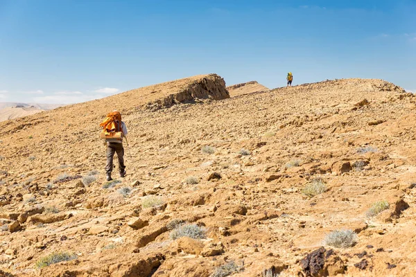 Två backpackers promenader stigande mountain rock desert lutning. — Stockfoto