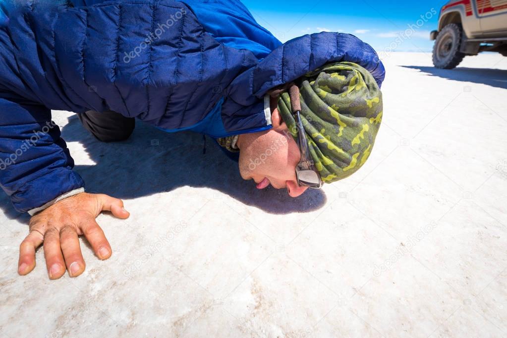 Guy licking salt surface Salar de Uyuni desert, Bolivia. 