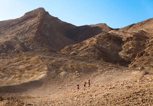 Tre backpackers promenader stigande mountain sten öken trail. — Stockfoto