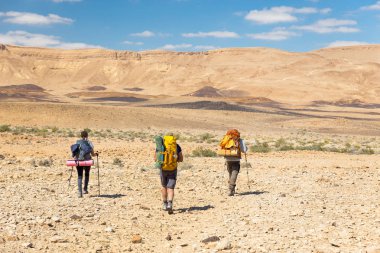 Üç backpackers taş yürüyüş iz çöl. 