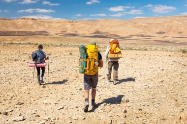 Üç backpackers taş yürüyüş iz çöl. 