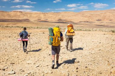 Three backpackers walking stone desert trail.  clipart