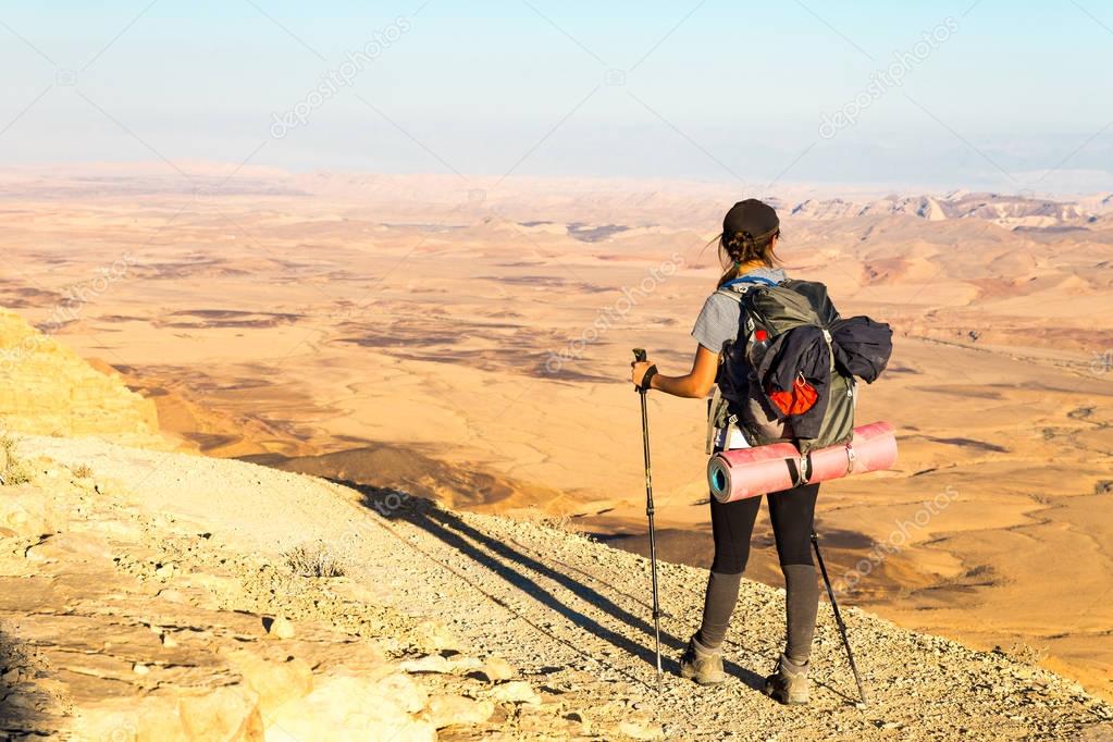 Young woman tourist backpacker standing looking view desert mountain edge