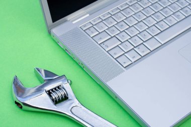 Yeşil arka planda gümüş bir dizüstü bilgisayarın yanına ayarlanabilir anahtar