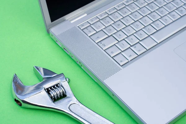 Chave ajustável ao lado de um laptop prateado em um fundo verde — Fotografia de Stock