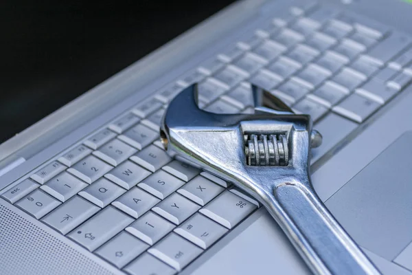 Verstelbare sleutel naast een zilveren laptop. Computerservice, onderhoudsthema. — Stockfoto