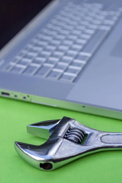 Chave ajustável ao lado de um laptop prateado. Serviço de computador, tema de manutenção . — Fotografia de Stock