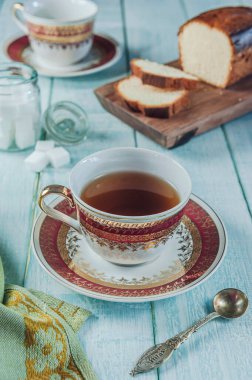 Kesme tahtasına dilimlenmiş bir pasta, küp şekerler ve porselen bir fincan te ile açık yeşil ahşap masa.