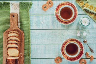 Açık yeşil ahşap arka planda dilimlenmiş pasta, şeker küpleri ve porselen bir fincan çay.