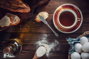 Dilimlenmiş ekmekle ahşap masa ve bir fincan çay.