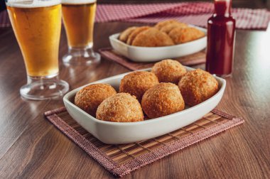 Brezilya aperatifi bol yağda kızartılmış peynirli kroket ve iki bardak bira ve acı biber sosu Bolinha de queijo.