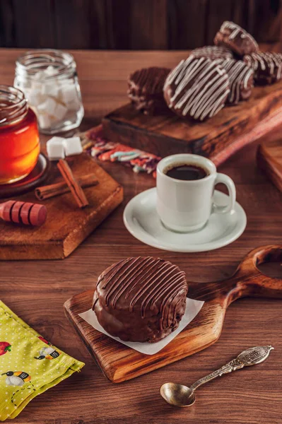 A bitten brazilian honey cookie chocolate covered on the wooden table with a porcelain cup of tea, honey bee and cinnamon - Pao de mel