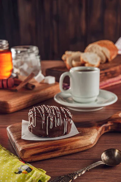 A bitten brazilian honey cookie chocolate covered on the wooden table with a porcelain cup of tea, honey bee and cinnamon - Pao de mel