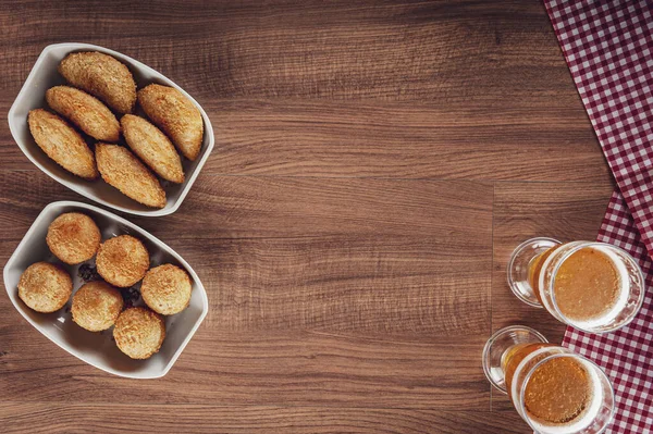 Brezilya aperatifi bol yağda kızartılmış peynir ve iki bardak birayla birlikte sığır kroket Bolinha de queijo ve risolis de carne uzay kopyasıyla üstte.