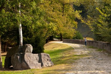 Bir kız, güneşli bir sonbahar gününde Borgonuovo 'daki Acquafraggia şelalelerinde bir patika boyunca yürür.