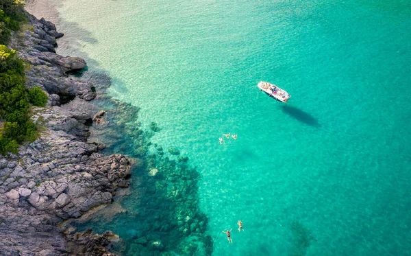 Légi kilátás Trsteno strand Montenegróban, közel Budva, egy hajó egy gyönyörű öbölben sziklás part, kék víz, az emberek fürödni tiszta vízben — Stock Fotó