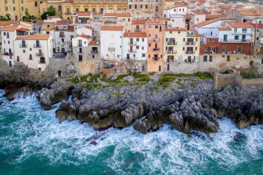 Kayalık sahilin ve Cefalu 'nun evlerinin rüzgarlı ve fırtınalı havalarda havadan görünüşü. Büyük dalgalar taşlara çarpar. Sicilya, İtalya