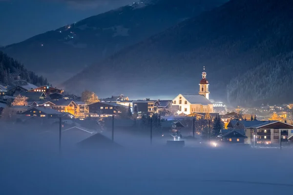 冬季的夜景俯瞰着奥地利的提洛里亚城市Neustift和普法尔教堂，背景是群山和云彩。 寒冷的夜晚，雾气弥漫山谷 — 图库照片