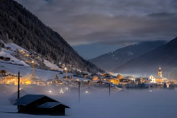 Winter night landscape overlooking the Austrian Tyrolean city of Neustift and the Pfarre church against the backdrop of mountains and clouds. Frosty night with fog in the valley — Stock Photo, Image