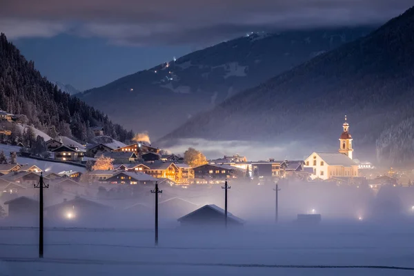 冬季的夜景俯瞰着奥地利的提洛里亚城市Neustift和普法尔教堂，背景是群山和云彩。 寒冷的夜晚，雾气弥漫山谷 — 图库照片