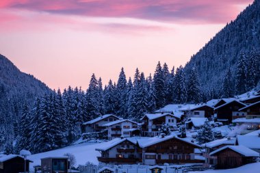 Tipik bir Avusturyalı köyü kış sabahı gün doğumunda. Karlı Orman Ağaçları ve Tirol Evleri