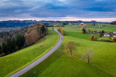 Miesbach yakınlarındaki Bavyera 'da sonbahar manzarası. Uzağa giden yol ve ufuktaki Alpler 'in zirveleri. Bulutlar gökyüzü, sarı ağaçlar ve yeşil alan