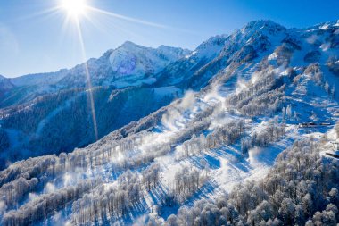 Rusya 'nın Sochi kentindeki Rosa Khutor kayak merkezindeki Kış Dağı manzarası. Donmuş ağaçlar, soğuk bir sabahta güzel bir sabah gökyüzüne karşı. Kar topları yamaçlara kar yağdırır.