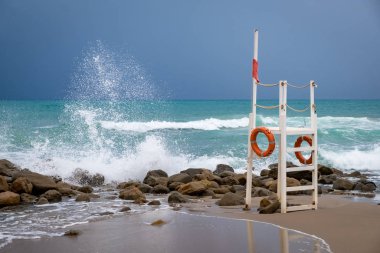 Fırtına sırasında Cefalu 'da boş bir sahilde cankurtaran kulesi. Taş sahili, dalgalardan fışkıran su, mavi su. Sicilya, İtalya