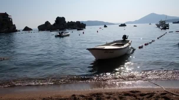 Pohled na rybářskou loď na pláži Przhno v Černé Hoře při západu slunce. Sluneční paprsky se krásně odrážejí od vody — Stock video