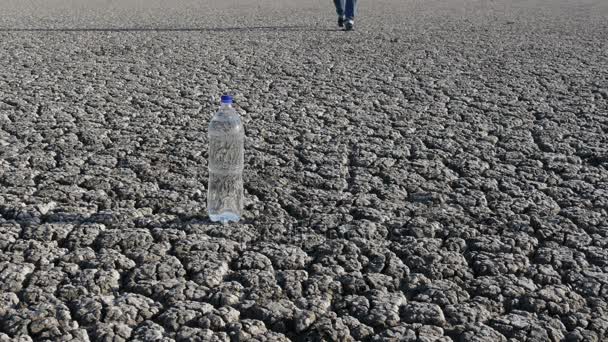 Άνθρωπος Περπατώντας Στην Ξηρά Ραγισμένη Και Πάρει Μπουκάλι Νερό — Αρχείο Βίντεο