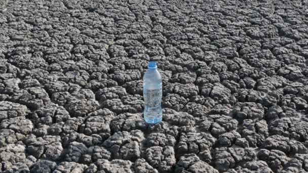 男は乾燥ひび割れ土地の上を歩くと水の瓶を拾う — ストック動画