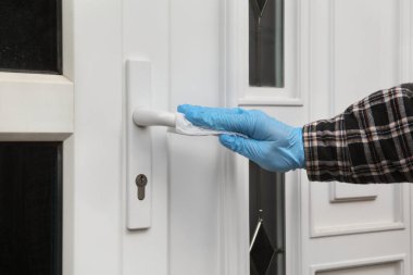 Koruyucu eldivenli insan eli antibakteriyel ya da temizlik çözeltisi ve ıslak mendil kullanarak evin kapı kolunu temizliyor.