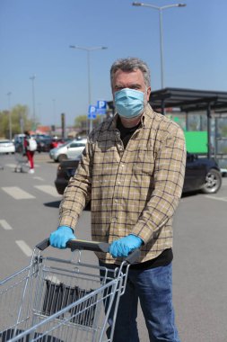 Koruyucu eldivenli ve maskeli bir adam alışveriş arabaları, korona virüsünün temel koruması