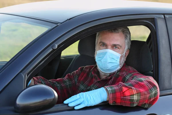 Adult driver with protective surgical mask and gloves sitting in a car, corona virus protected person